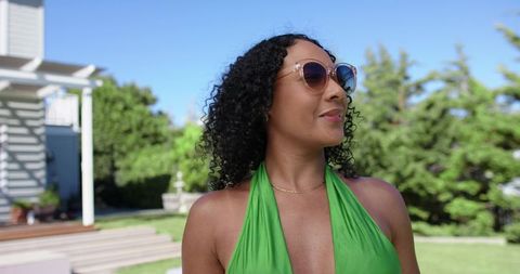 African american woman enjoying sunny backyard in green halter top and stylish sunglasses