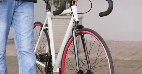 Man holding white road bicycle with red rim wheel on urban sidewalk near planter