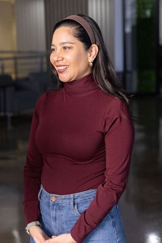 Smiling professional woman wearing maroon turtleneck and denim jeans in lobby
