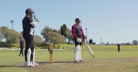 Cricket Players Strategizing on Field During Sunny Day Match