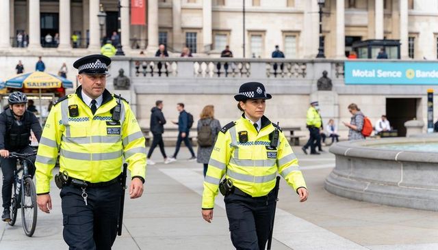 Uniformed police officers patrolling city plaza in high-visibility jackets near fountain