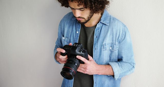 A young Caucasian man reviews images on his digital camera, with copy space. His focused expression and casual attire suggest he might be a photography enthusiast or a professional reviewing his work.