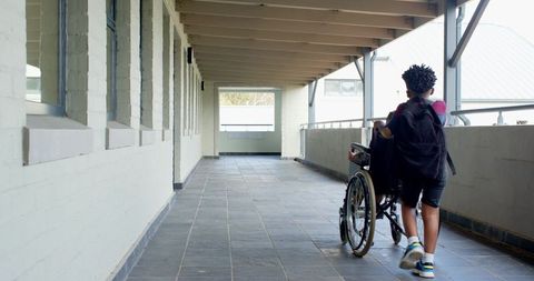 Inclusive school friendship journey in hallway, pushing wheelchair