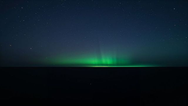 Glowing Aurora Borealis Ribbon Dancing Above Dark Ocean Horizon Under Starry Sky