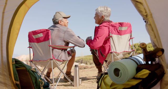 Back view of happy diverse senior couple sitting and talking on camping in mountains. Retirement, vacations, togetherness, summer, active senior lifestyle, unaltered.