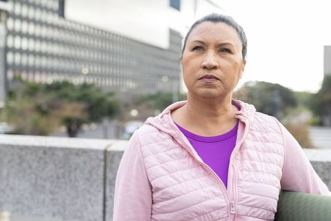 Mature woman leaning on concrete wall reflecting in urban plaza during overcast morning