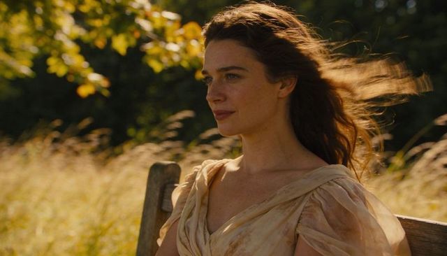 Serene woman sitting on bench in sunlit meadow wearing flowing pale dress, golden hour