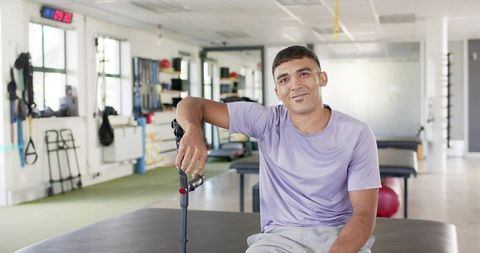 Smiling man sitting with forearm crutch on treatment table in bright rehabilitation clinic