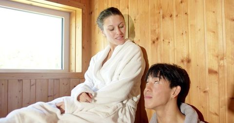 Sunlit spa couple relaxing in wooden sauna wearing robes and towel serene wellness retreat