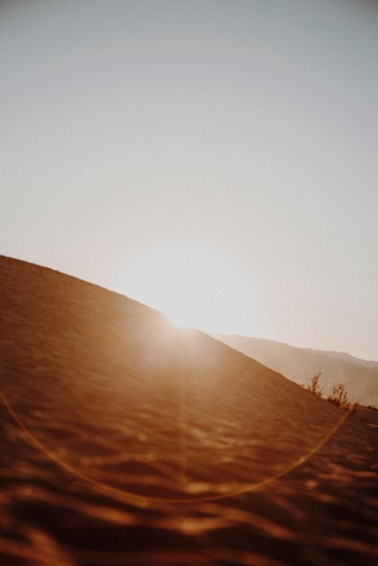 This photo captures a beautiful sunset over desert sand dunes with a striking lens flare. Suitable for travel blogs, environmental websites, or inspirational content emphasizing natural beauty. The minimalistic yet serene setting can also enhance backgrounds for motivational quotes or meditation guides.