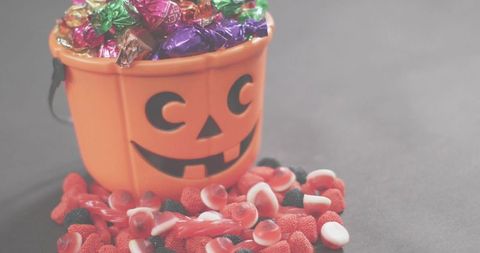 Jack-o'-lantern bucket spilling colorful foil-wrapped candies and gummies on dark table