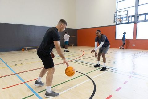 Diverse men practicing one-on-one basketball dribbling on indoor court with gym light