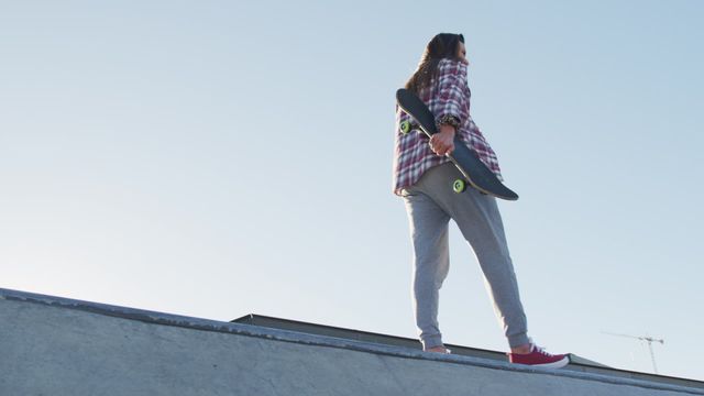 This scene captures a female skateboarder casually walking along a skateboard ramp, with the skateboard held behind her. Ideal for representing youthful lifestyle, urban culture, and opportunities for an active and spirited leisure activities concept.