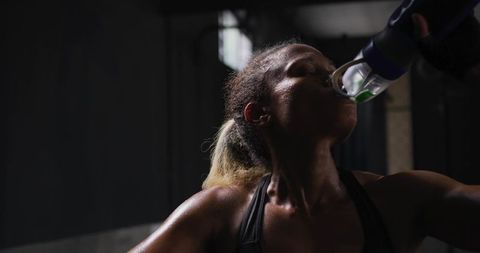 Athlete Drinking Water After Workout in Dark Gym Environment