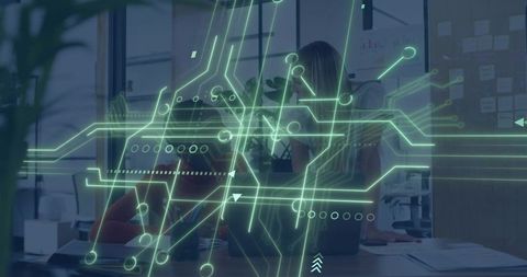Two women collaborating over laptop with neon-green circuit overlay in open office