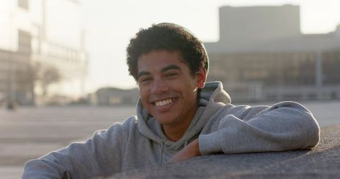 Sunlit african american young man smiling in gray hoodie leaning on urban ledge