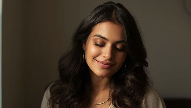 Serene woman closing eyes and smiling in warm soft-light closeup with gold jewelry
