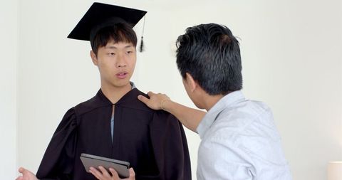 Father congratulating son in graduation gown with a tablet