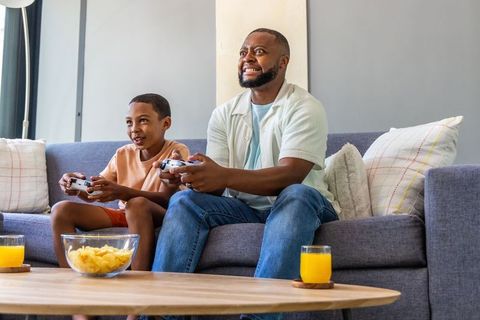 African american father and son competing during intense couch gaming session with snacks