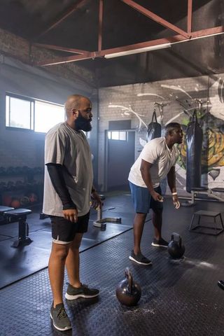 Two african men coaching partner kettlebell workout in industrial brick gym interior