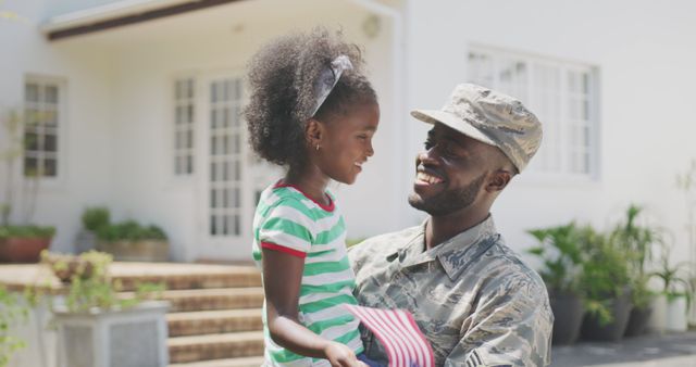 Military father reuniting with daughter, both smiling and embracing in front yard of home. Suitable for themes of military families, homecoming celebrations, family bonds, and pride. Perfect for use in military support advertisements, family-themed campaigns, and homecoming stories.