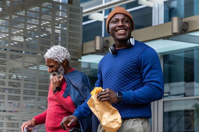 African american men walking downtown wearing knits and beanie, holding pastry and coffee