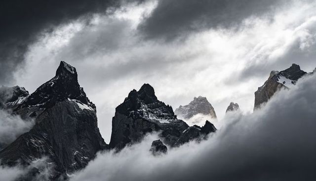 Towering jagged alpine spires rising above foggy valleys, snow-scarred ridges, moody light