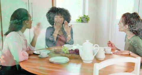Friends enjoying sunlit tea and laughter around wooden table in cozy home kitchen