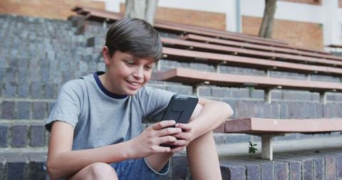 Smiling School Boy Engaging with Smartphone on Bleacher Steps