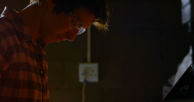 A craftsman is deeply engrossed in his work in a dimly lit workshop. He is wearing safety glasses and appears to be working on a detailed project, reflecting focus and dedication. This image can be used for websites or articles related to craftsmanship, DIY projects, skilled trades, or safety in manual work settings.