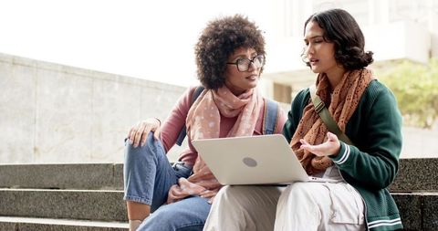 Diverse Female Students Collaborating on Laptop Outdoors on Campus Steps Discussing Project