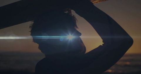 Surfer standing holding surfboard overhead at sunset with lens flare silhouette
