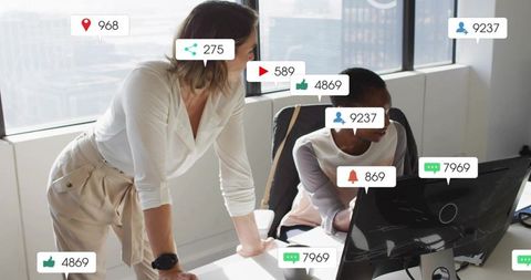 Female coworkers collaborating on social media analytics at modern office desk