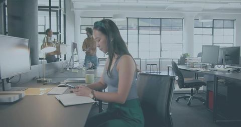 Young woman using smartphone at modern open-plan office desk with natural light