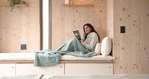 Relaxed Woman Reading on Cozy Indoor Bench with Blanket