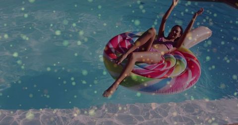 Relaxing woman floating on colorful donut pool float in sunny blue pool