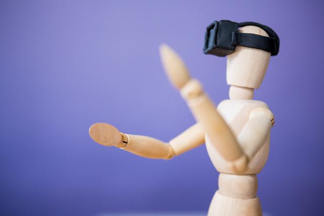 Close-up of a wooden mannequin wearing a virtual reality headset, set against a purple background. This can be used to symbolize technology, innovation, and the future of immersive digital experiences. Ideal for articles, presentations, and marketing materials related to VR technology, digital innovation, and modern gadgets.