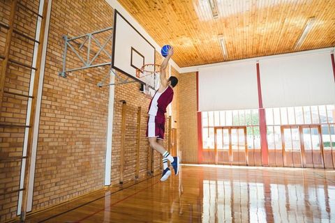Dunking basketball in school gymnasium by athletic young man