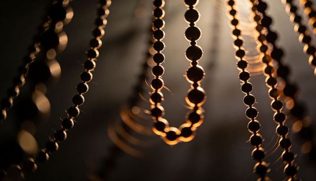 Macro backlit metallic bead strands capturing warm rim light and dusty texture