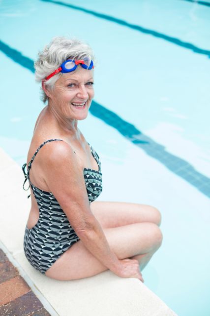 Senior woman sitting on poolside in swimsuit, smiling at camera. Ideal for promoting active lifestyle, senior fitness, health and wellness, leisure activities, and summer fun.