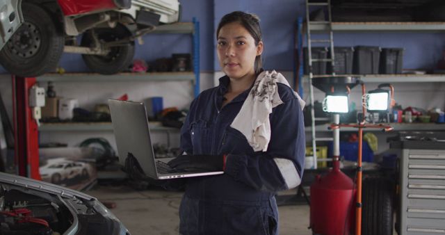 Portrait of female mechanic using laptop and smiling at a car service station. automobile repair service