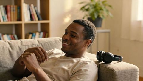 Relaxing man reclining on sofa with headphones, smiling in sunlit cozy living room