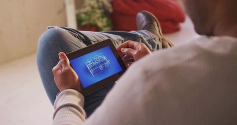 Man holding tablet viewing 3d house blueprint wireframe in cozy living room