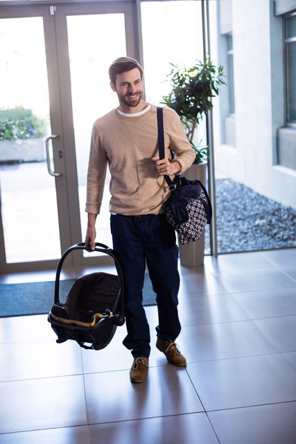 Smiling man holding baby carrier and bag in hospital