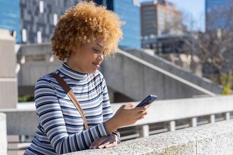 African american woman checking phone while leaning on urban plaza railing in daylight