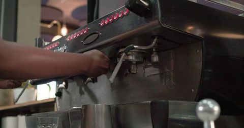 Barista attaching portafilter on commercial espresso machine preparing milk pitchers
