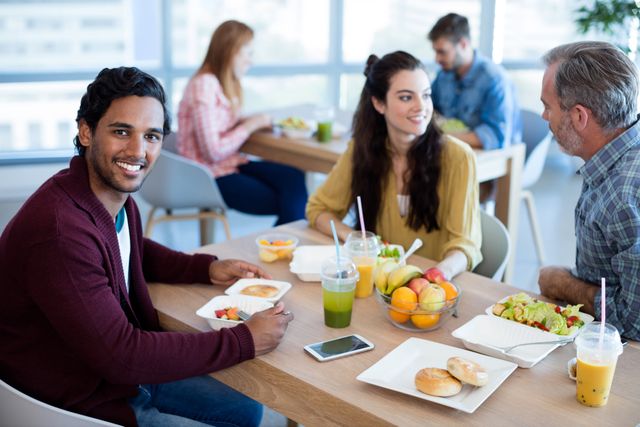Group of colleagues enjoying a meal together in a bright office cafeteria. Ideal for illustrating workplace culture, team bonding, and healthy eating habits in a professional setting. Useful for corporate websites, HR materials, and articles on work-life balance.