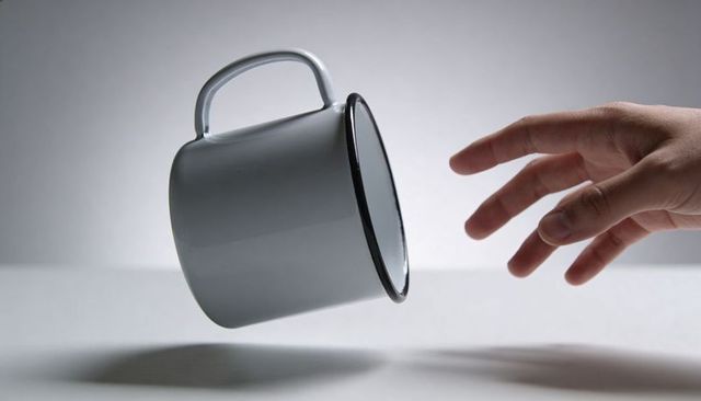Levitating white enamel mug with hand reaching to catch, minimal gray composition