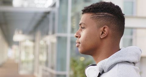 Young african american man gazing in glass corridor with hoodie and headphones — urban profile