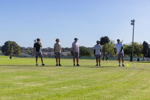 Five male teammates standing on grass field preparing for training drill in suburban park